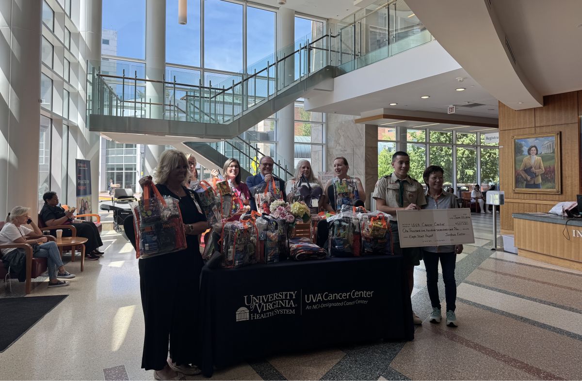 Group of people stand behind a table full of gift baskets in a bright hospital lobby, with a UVA Cancer Center sign on the table.