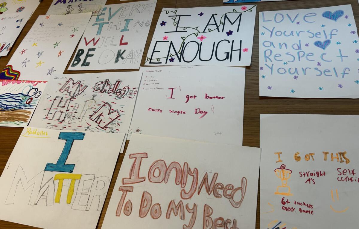 Collection of handmade posters with positive affirmations like 'I am enough' and 'Love yourself' displayed on a table surface, colorful markers and drawings visible.