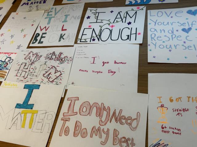 Collection of handmade posters with positive affirmations like 'I am enough' and 'Love yourself' displayed on a table surface, colorful markers and drawings visible.