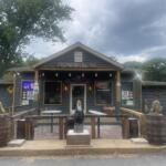 Exterior of Royals of Troy with an open sign, rustic outdoor seating, and wooden barrels under a cloudy sky.
