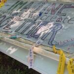 Handmade banner laid over a folding table with colorful, large lettering promoting a message about peace, freedom, and imagining a better world; markers and fabric scraps are nearby.