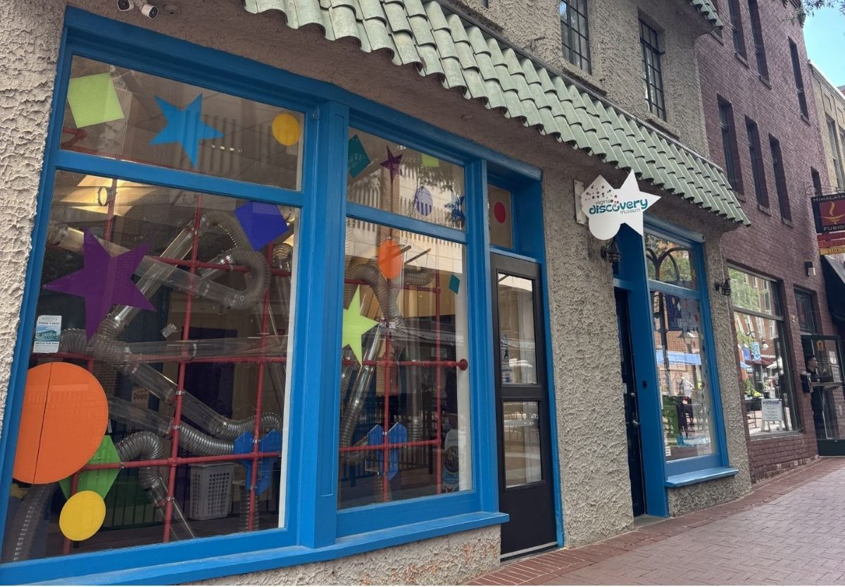 Front of the Discovery Museum with bright blue window frames and colorful star shapes on the glass; ducts and tubes visible inside.ans