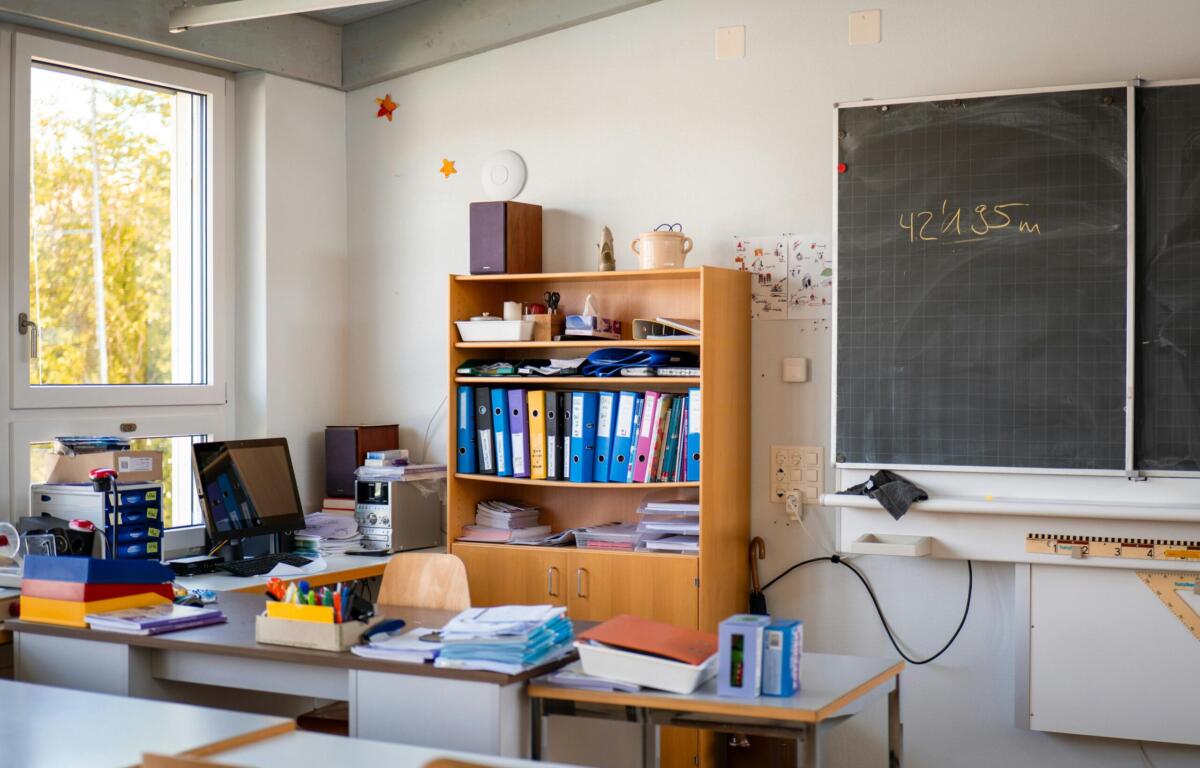 Bright classroom corner with a wooden shelf full of binders, papers, and a chalkboard to the right.
