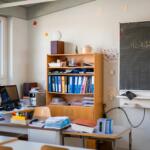 Bright classroom corner with a wooden shelf full of binders, papers, and a chalkboard to the right.