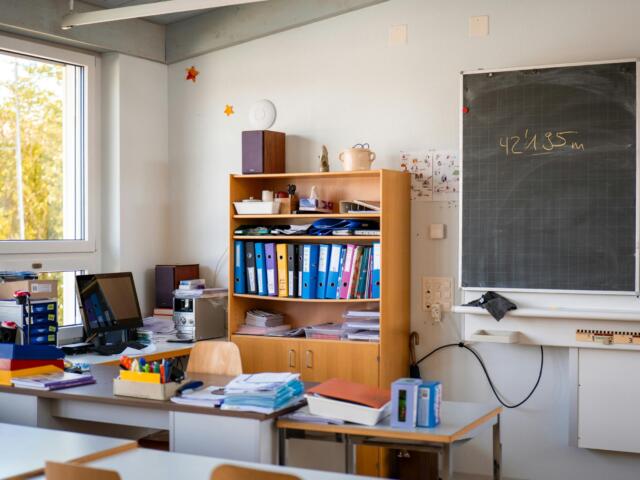 Bright classroom corner with a wooden shelf full of binders, papers, and a chalkboard to the right.