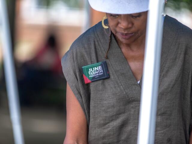 Person wearing a gray sleeveless top with a badge reading 'June Teenth Freedom Day' pinned to the chest.