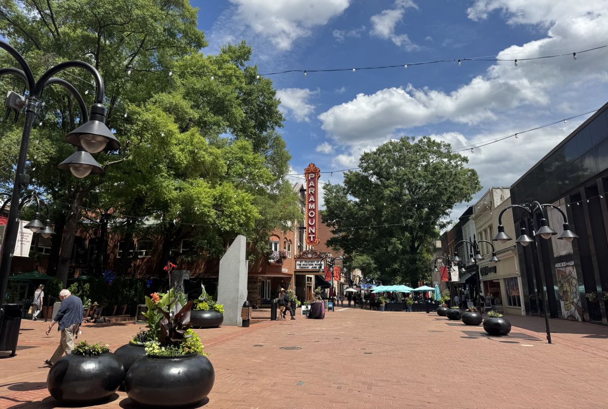 Downtown pedestrian street with a tall Paramount theater sign, string lights, and outdoor seating under umbrellas, daytime.