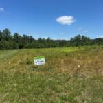 Open grassy field with a small sign reading 'Landscape Restoration in Progress' and trees on the horizon.