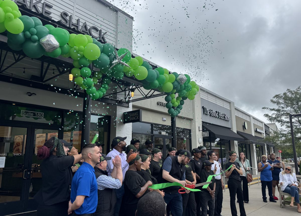 Ribbon cutting ceremony outside Shake Shack with a green balloon arch, confetti, and cheering attendees.