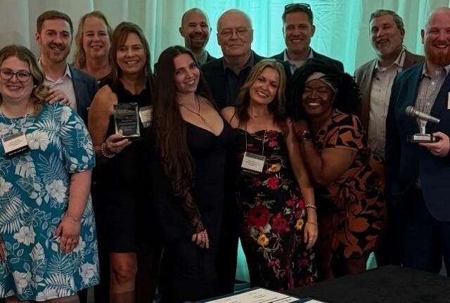 Group of smiling professionals posing at an awards ceremony; several hold plaques with a teal backdrop behind them.