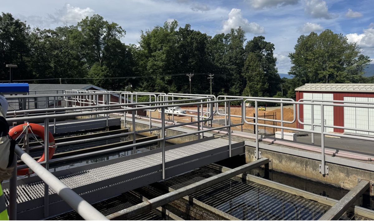 Industrial water treatment plant with metal catwalks, railings, and a red lifebuoy, trees in the background on a sunny day.
