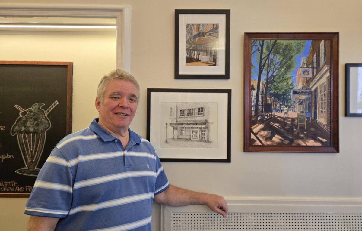 Smiling man in a blue striped polo standing beside framed artworks on a gallery wall.