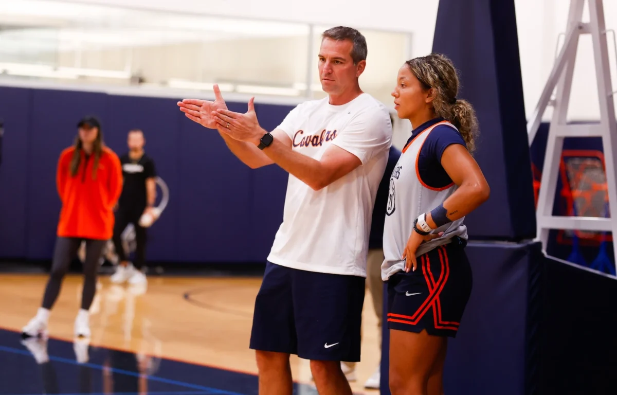 Male basketball coach explains a play to a female player by the sideline during practice in a gym edge of the court.