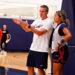 Male basketball coach explains a play to a female player by the sideline during practice in a gym edge of the court.