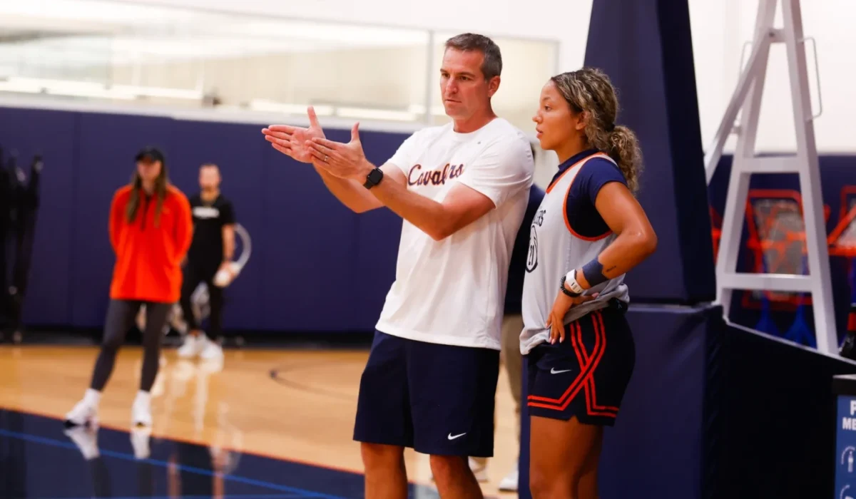 Male basketball coach explains a play to a female player by the sideline during practice in a gym edge of the court.