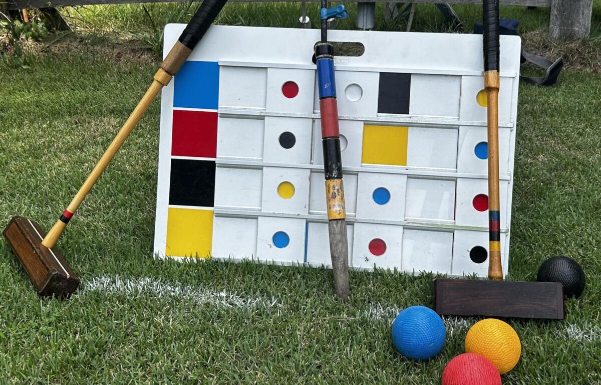 Giant outdoor Connect Four-style board on grass with colorful balls nearby and wooden mallets resting against it.