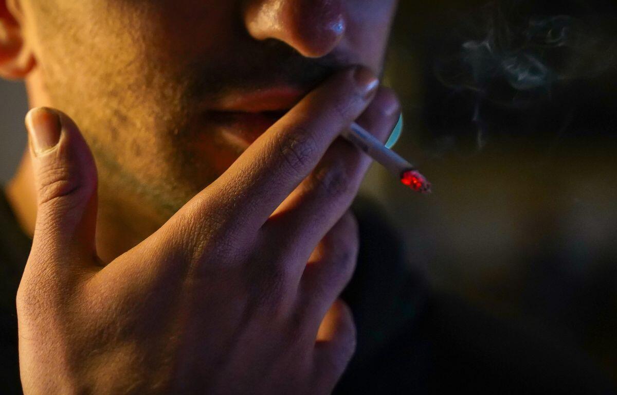 Close-up of a person smoking a cigarette, ember glowing as it rests near their lips in low light.