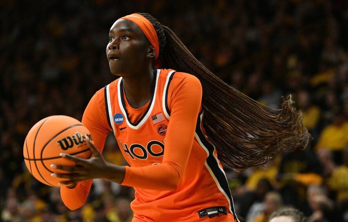 Female basketball player in an orange jersey drives toward the basket, gripping an orange basketball with both hands as her long braids swing behind her.