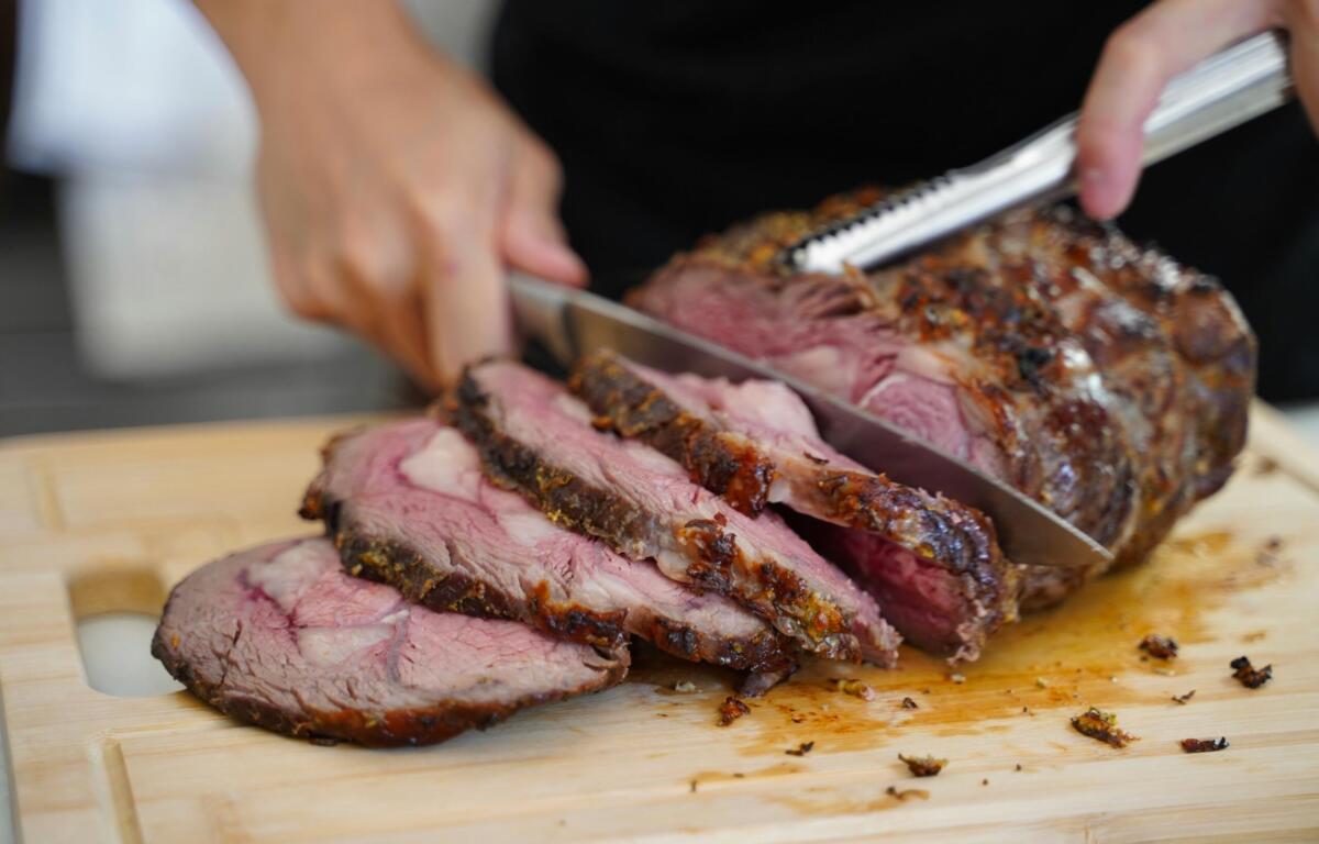 person carving roast beef on a cutting board