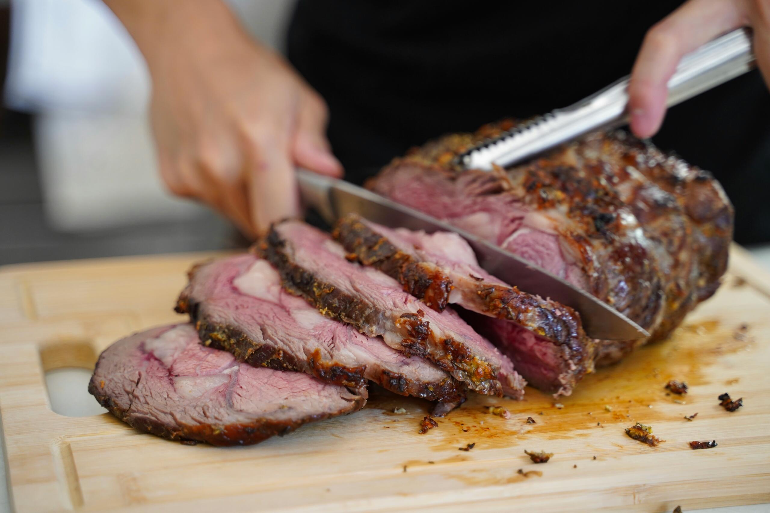 person carving roast beef on a cutting board