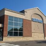 Kroger grocery store exterior with large blue Kroger sign, brick and beige facade, and glass windows under a clear blue sky.