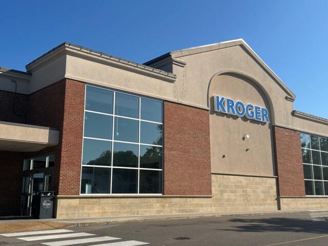 Kroger grocery store exterior with large blue Kroger sign, brick and beige facade, and glass windows under a clear blue sky.