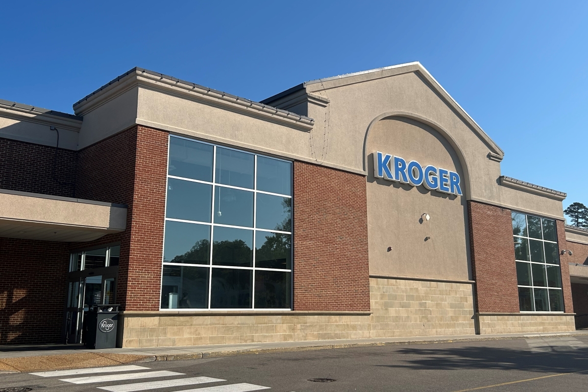 Kroger grocery store exterior with large blue Kroger sign, brick and beige facade, and glass windows under a clear blue sky.
