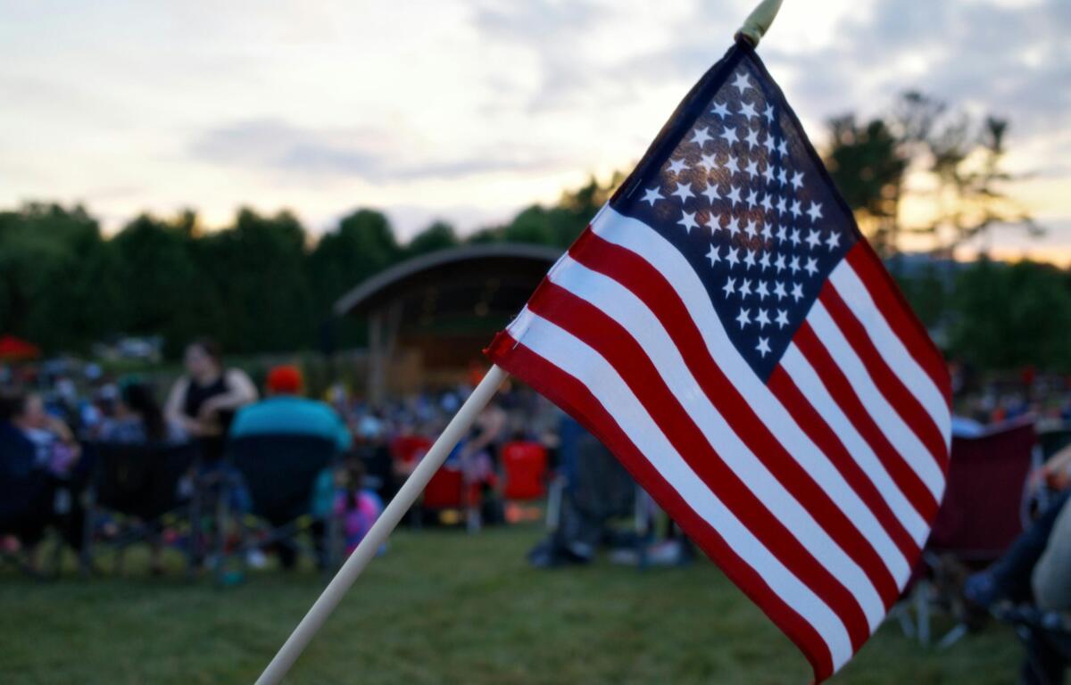 American flag on a pole waved at an outdoor gathering with people blurred in the background