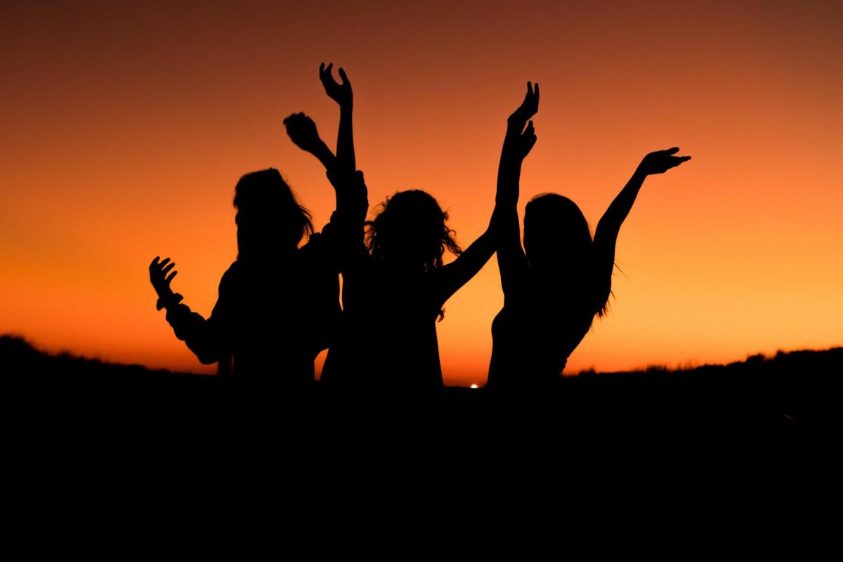 three women's silhouettes jumping in front of an orange sky as the sun sets