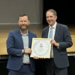 Director of Bands Jason Hackworth (left) accepts the official invitation to the parade from Deputy Lieutenant for Greater London Steve Summers (right).