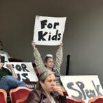 Daisy Rojas holds up a sign during an Albemarle County School Board meeting