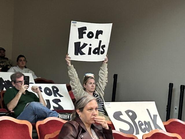 Daisy Rojas holds up a sign during an Albemarle County School Board meeting