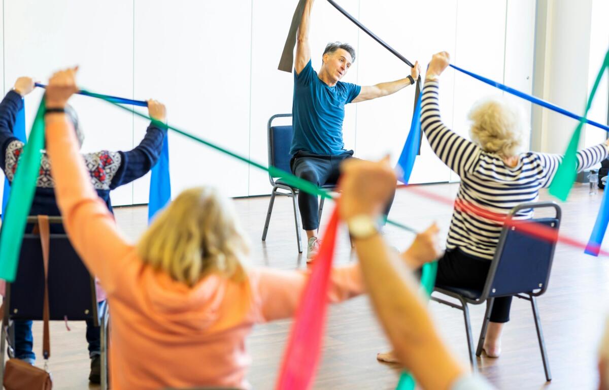 senior exercise class sitting in seats with resistance bands