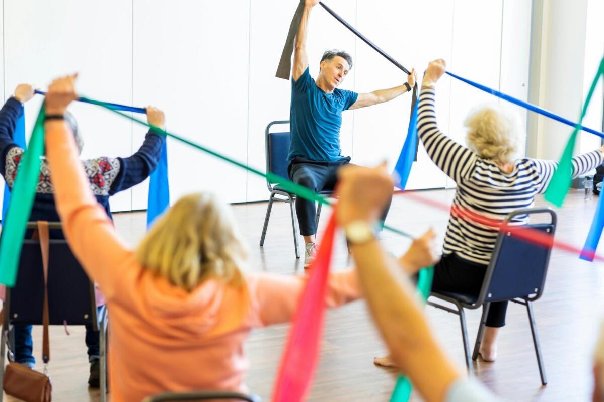 senior exercise class sitting in seats with resistance bands